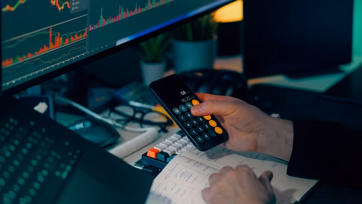Analyst using a calculator at a desk with computer charts
